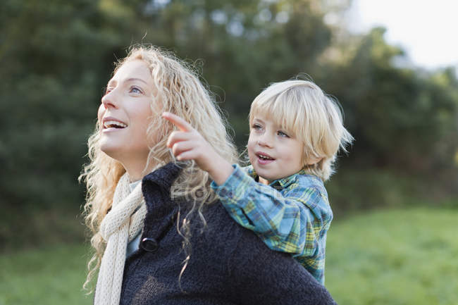 Mother carrying son piggyback outdoors — Stock Photo