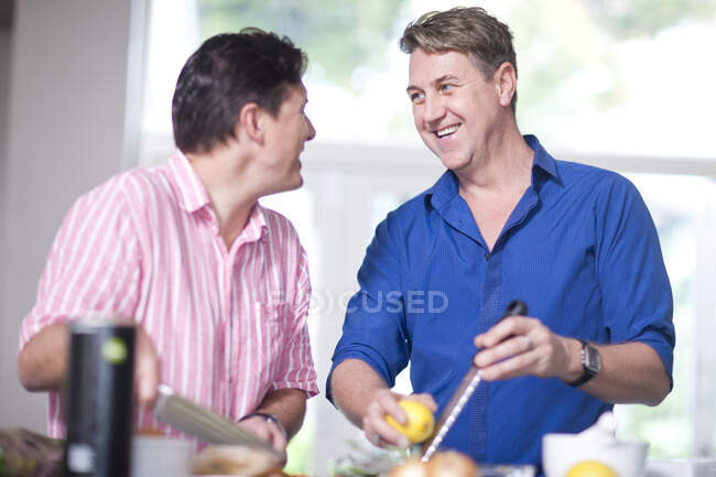 Mature men in kitchen, one grating lemon zest — Stock Photo