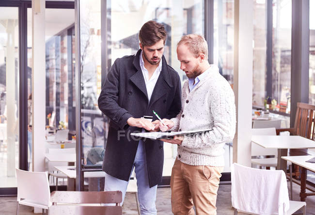 Dos jóvenes empresarios se reúnen en la cafetería escribiendo en cuaderno - foto de stock