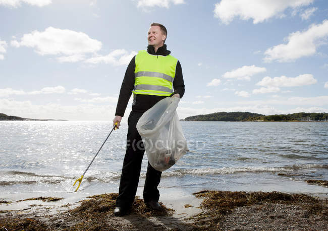Lavoratore in giubbotto di sicurezza pulizia spiaggia — Foto stock