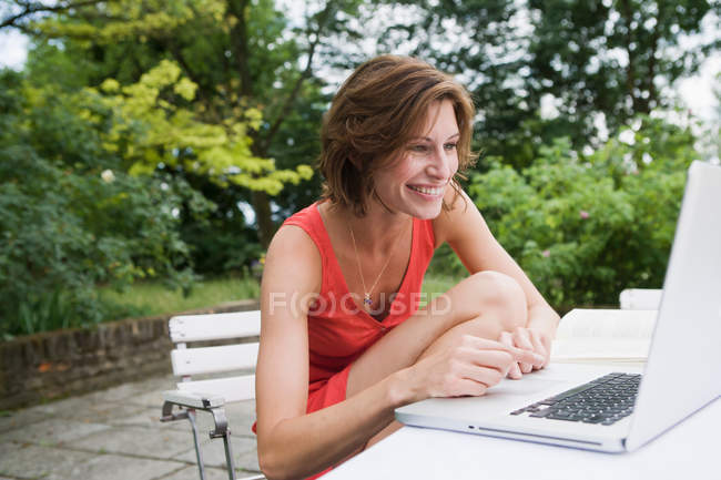 Усміхнена жінка використовує ноутбук на задньому дворі — стокове фото