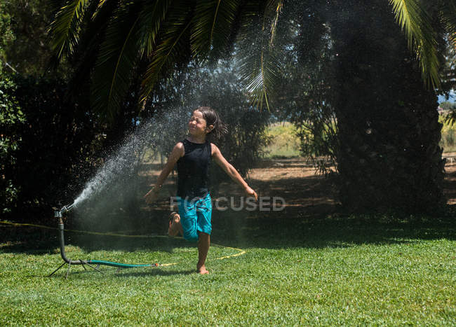 Мальчик бежит по воде из садового разбрызгивателя — стоковое фото