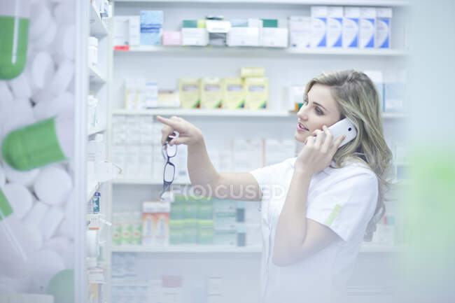 Farmacéutico en la llamada telefónica y apuntando a la medicación - foto de stock