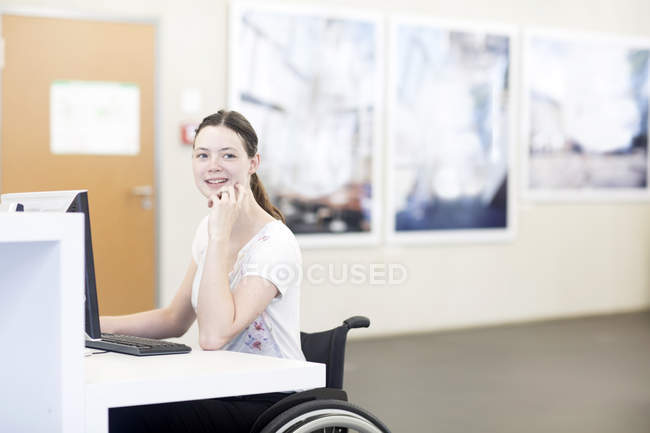 Молодая студентка университета в инвалидной коляске за компьютером за столом — стоковое фото