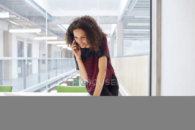 Designer feminino lendo laptop e falando no smartphone em estúdio de design — Fotografia de Stock