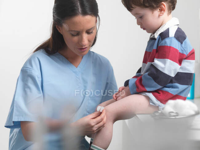 Nurse applying bandage to boys knee — Stock Photo