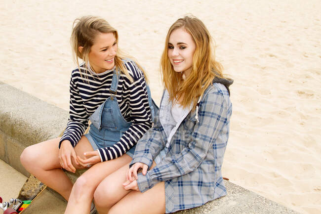 Girlfriends sitting on wall at beach — Stock Photo