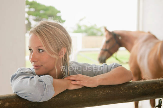 Woman leaning against stable gate — Stock Photo