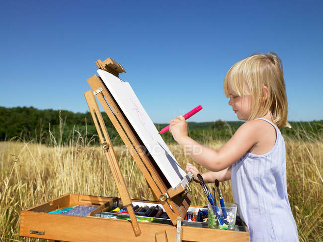 Chica pintando en un campo - foto de stock