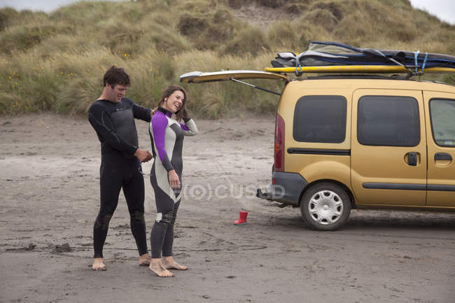 Homem ajudando mulher colocando terno molhado na praia — Fotografia de Stock
