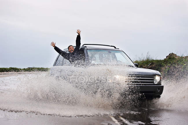 Man leaning out of splashing car — Stock Photo