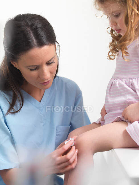 Enfermeira aplicando bandagem no joelho das meninas — Fotografia de Stock
