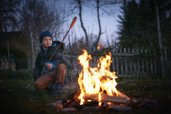 Boy toasting marshmallows on garden campfire at dusk — Stock Photo