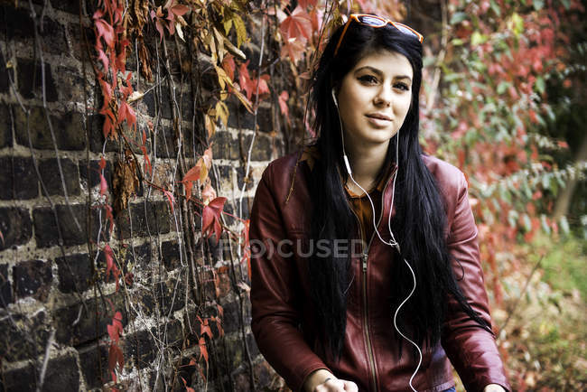 Portrait de jeune femme assise à l'extérieur, portant des écouteurs — Photo de stock