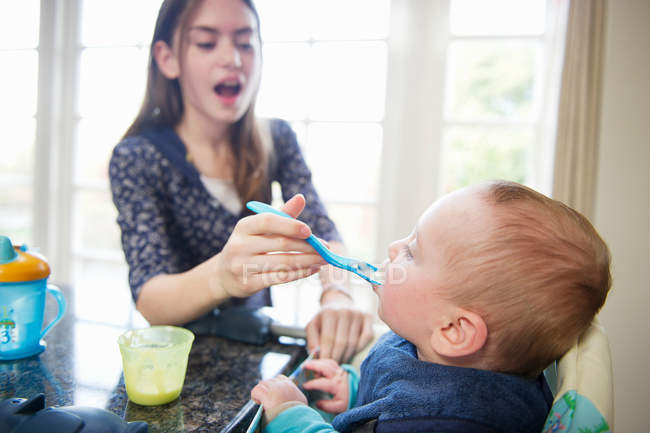Menina alimentando bebê irmão à mesa — Fotografia de Stock