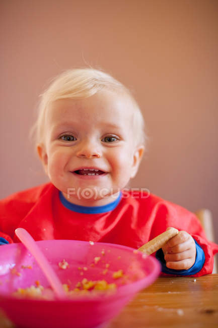 Smiling baby girl eating at table — Stock Photo