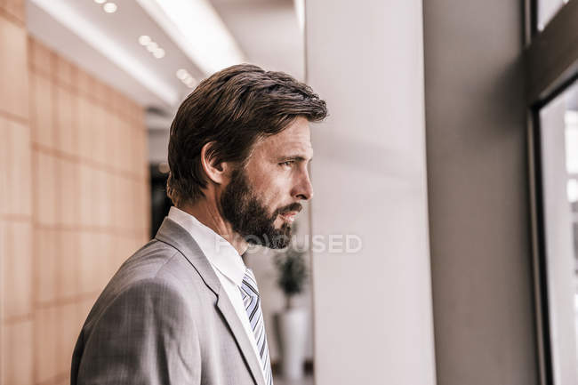 Vista lateral del hombre de negocios barbudo mirando por la ventana - foto de stock
