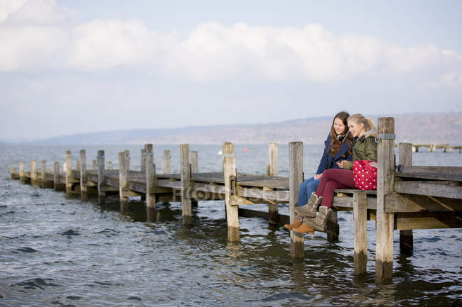 Two teenage girls sitting on wooden jetty — Stock Photo