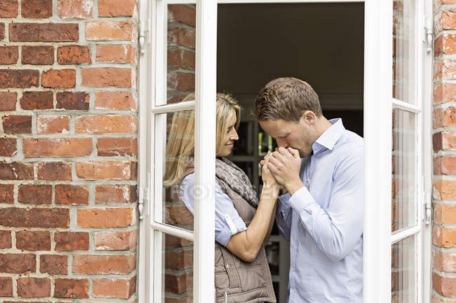 Casal adulto médio pela janela, homem beijando as mãos da mulher — Fotografia de Stock