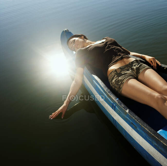Woman in camouflage shorts lying in blue boat at lake — Stock Photo