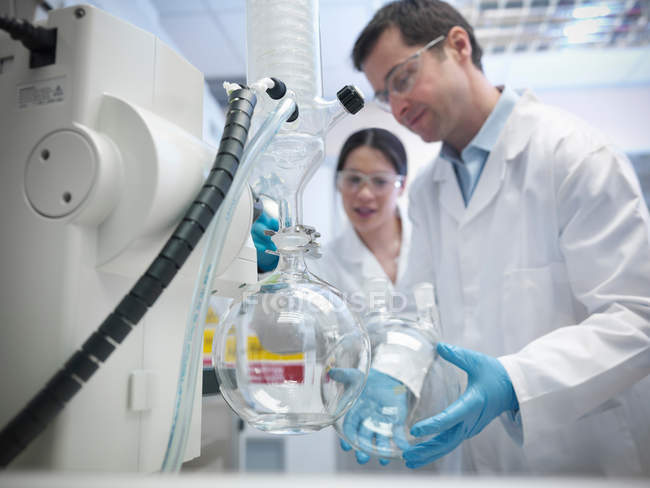 Científicos masculinos y femeninos que trabajan con vacío aún en laboratorio, científicos masculinos sosteniendo recipiente de vidrio - foto de stock