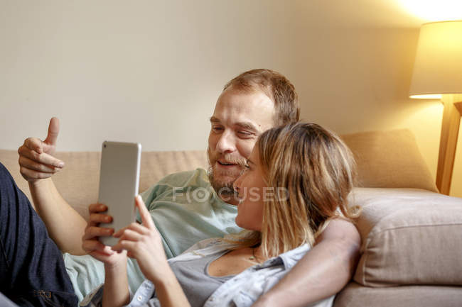 Pareja adulta media relajándose en el sofá, mirando la tableta digital - foto de stock