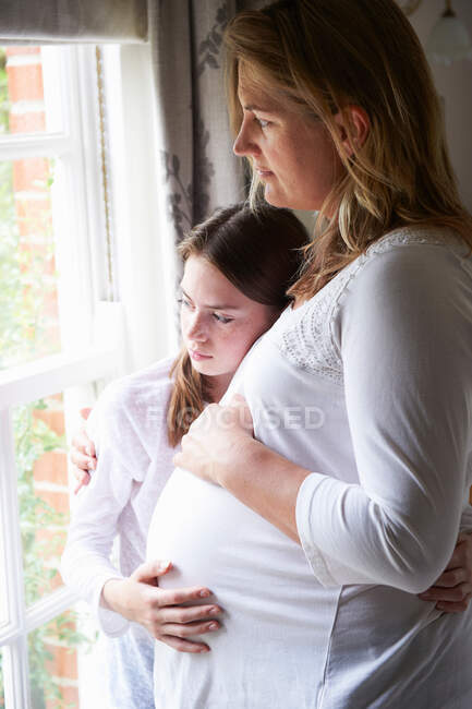Pregnant mother with teenage daughter looking through window — Stock Photo