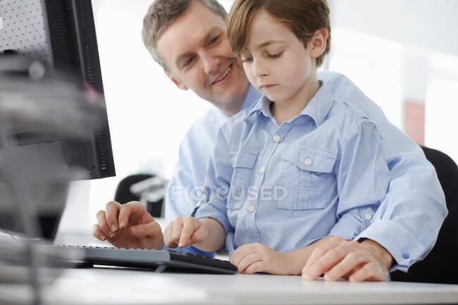 Niño sentado en el regazo del padre usando el teclado de la computadora - foto de stock