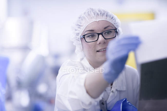 Trabalhador da fábrica usando rede de cabelo olhando para papelada — Fotografia de Stock