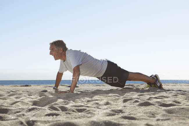 Homem sênior fazendo flexões na praia — Fotografia de Stock
