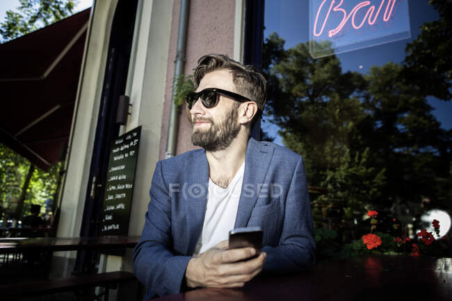 Hombre fuera del bar, sosteniendo teléfono inteligente sonriendo, Berlín, Alemania - foto de stock