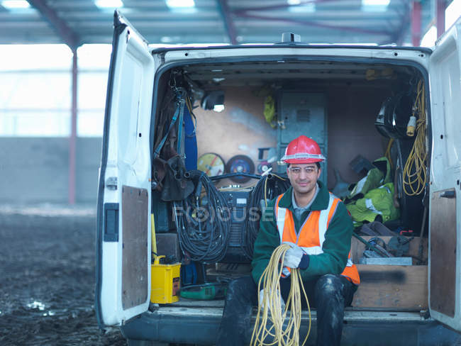 Portrait of construction worker holding cables in back of van on building site — Stock Photo