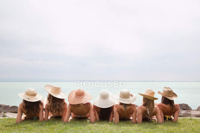 Mujeres con sombreros de paja se recuestan junto al lago - foto de stock