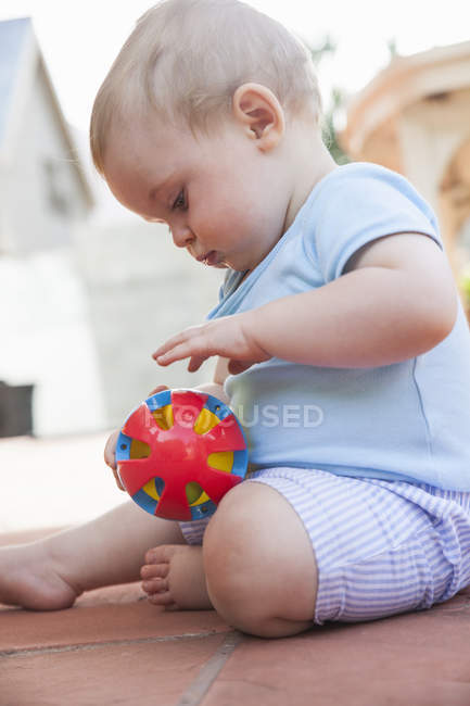 Малыш сидит на террасе и играет с игрушкой. — стоковое фото