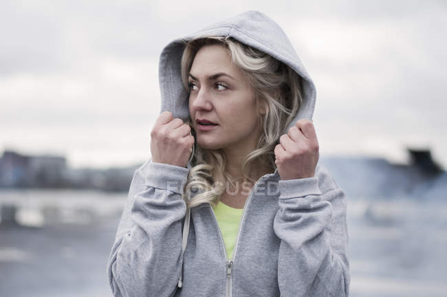 Femme coureuse mettant capuche sur quai pluvieux — Photo de stock