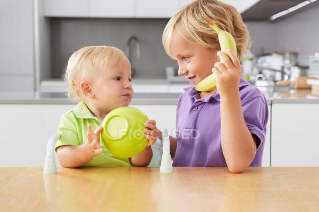 Brothers playing with bowl and banana at table — Stock Photo
