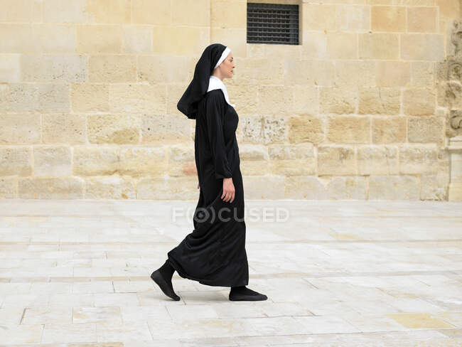 Монахиня идет перед каменной стеной — стоковое фото