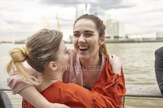 Zwei junge Geschäftsfrauen umarmen sich am Wasser, London, Großbritannien — Stockfoto
