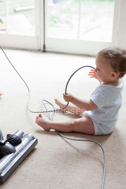 Baby on floor playing with hoover cable — Stock Photo