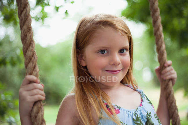 Menina sorridente sentado no balanço da árvore, foco em primeiro plano — Fotografia de Stock
