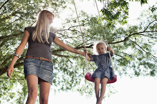 Madre empujando hija en swing - foto de stock