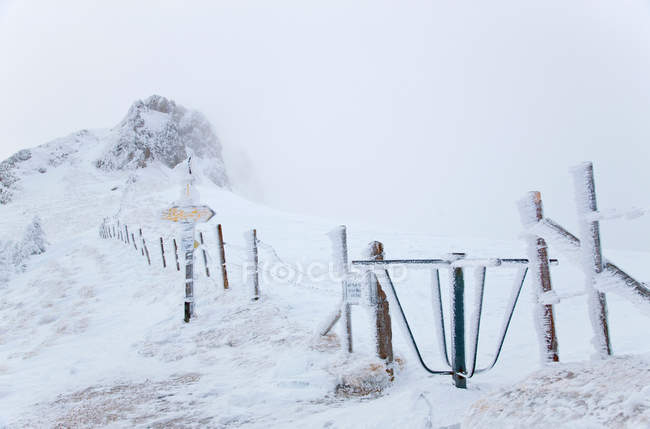 Cerca rural oscurecida por nieve y señal de dirección congelada - foto de stock