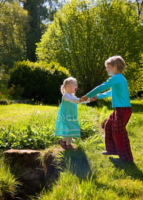 Мальчик помогает сестре пересечь ручей — стоковое фото