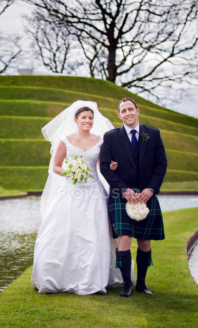Casal recém-casado andando na ponte gramada — Fotografia de Stock
