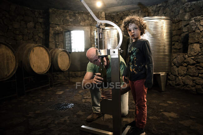 Menino com enólogo arrolhando garrafa de vinho na adega — Fotografia de Stock