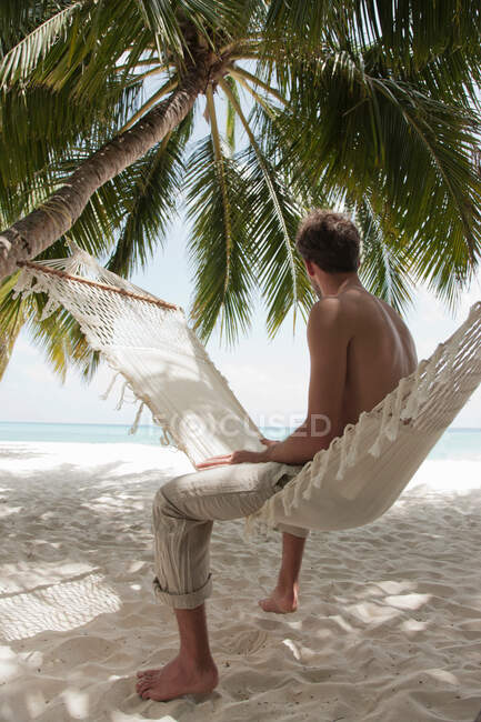 Человек сидит в гамаке на пляже — стоковое фото
