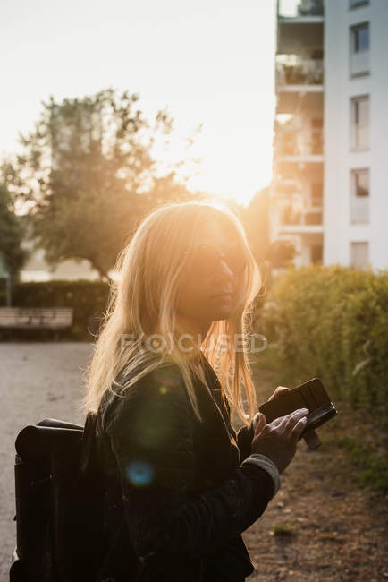 Jeune femme à l'extérieur, au coucher du soleil, en utilisant un smartphone — Photo de stock