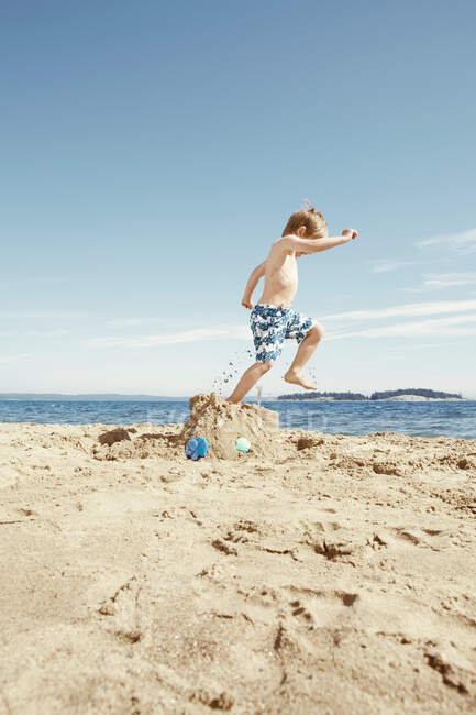 Chico pisando el castillo de arena en la playa - foto de stock