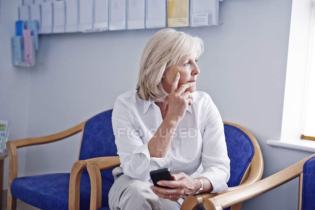 Reife Patientin mit Handy im Krankenhaus-Wartezimmer — Stockfoto