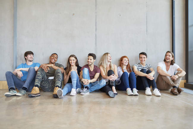Retrato de grupo de estudiantes masculinos y femeninos sentados en el piso en una fila en la universidad de educación superior - foto de stock